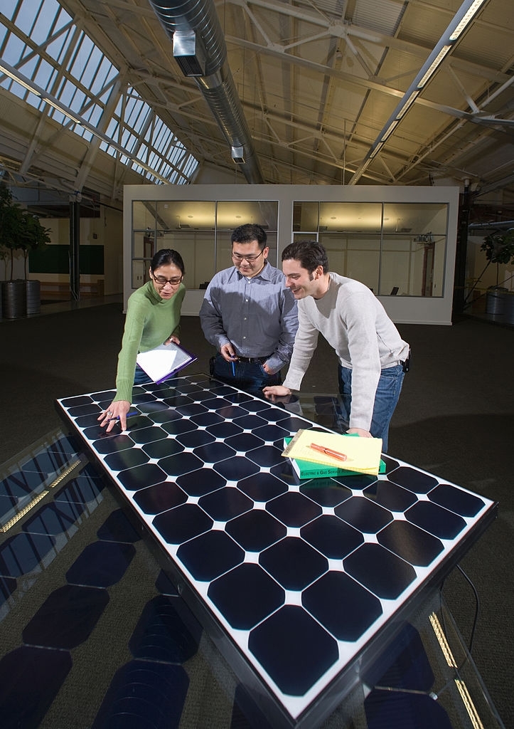 One woman and two men in a business meeting discussing a photo voltaic solar panel and alternative energy.